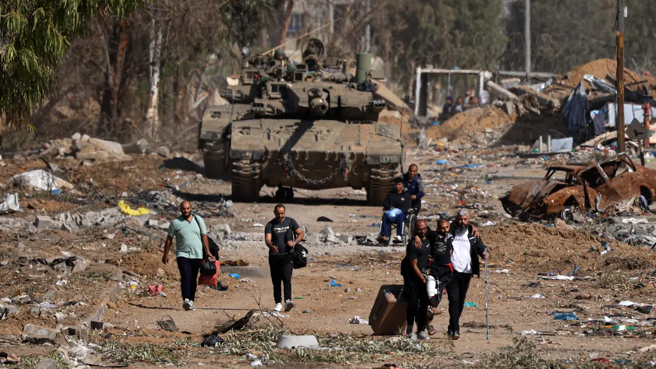 Warga Palestina yang melarikan diri dari utara melalui jalan Salaheddine di distrik Zeitoun di pinggiran selatan Kota Gaza berjalan melewati tank-tank tentara Israel pada 24 November 2023 setelah gencatan senjata selama empat hari yang dimulai sejak pagi hari.